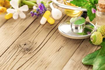 Obraz na płótnie Canvas Natural herbal medicine concept. Stethoscope with various plants, leaves of healing herbs, capsules and healthy oils on wooden table with copy space. Alternative medicine