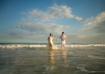 Fototapeta na wymiar couple in white running forward in water on beach.