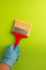 Female hand in blue gloves holds a red brush for painting on a green background. Repair concept. Flat lay