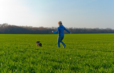 A girl and a dog run on the grass in the field.