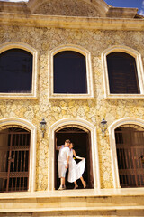 couple dressed in white, stands in arch of house.