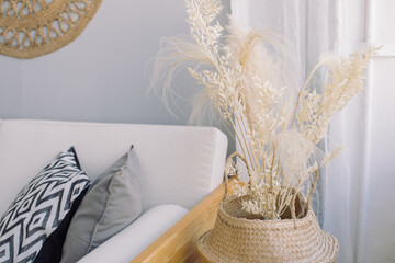 Cozy living room interior design concept. White sofa with pillows against gray wall and decorative plant in basket.