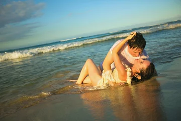 wet lovers lie on beach in water and kiss.  © andrey