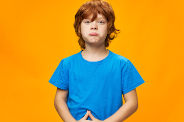 redhead boy The offended child pouted his lips blue t-shirt yellow background 