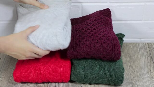 Neatly folded winter clothes. Folding sweaters in a pile.  Cozy sweaters are lying in a pile. A female hand on stacks warm sweaters in pile. Female stacking the warm sweaters into the pile. 