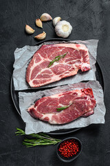 Raw pork steak. Marble meat on parchment paper. Black background. Top view
