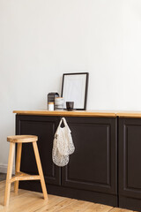 Modern cupboard with cotton bags and various decorations placed near wooden stool against white wall in stylish apartment