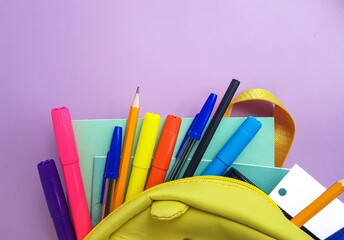 Fototapeta premium School yellow backpack with notebooks and school supplies on a purple background. Back to school.