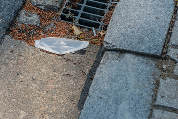 White medical mask discarded next to drainage grate