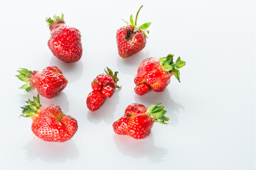Ugly bright red strawberries with reflection on a white glossy background.