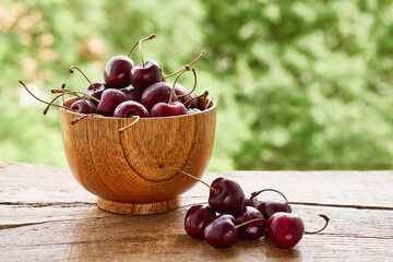 Wooden bowl of ripe, tasty, red cherries on a rustic wooden table
