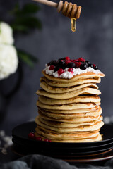 Pancake tower with fresh blueberry and mint, hand is keeping wooden stick pouring honey flow