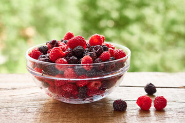 Glass bowl of delicious red and black raspberries on a wooden rustic table