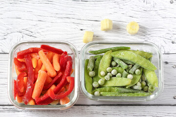 Frozen vegetables such as green peas, pea pods, green beans, red sweet pepper and baby carrot in the transparent bowls on the concrete wooden background with copy space, top view