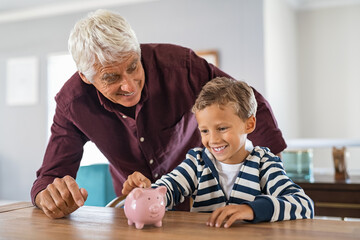 Child and grandfather saving money in piggybank