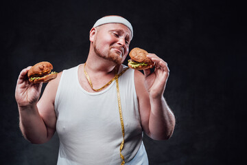 Fat men in sportswear, with a measure rope around his neck, holding two hamburgers and playing with them in a very funny way