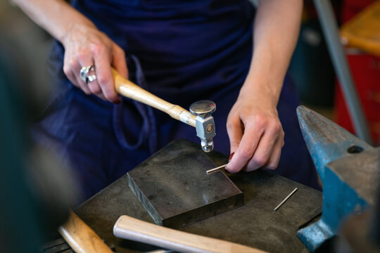 Crop craftswoman hitting silver part with hammer
