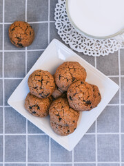 homemade crispy oatmeal cookies with chocolate on a square white plate on a gray tablecloth, a mug of milk close up