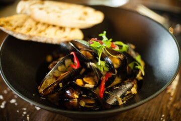 Blue mussels in white wine sauce in black bowl. Delicious healthy seafood closeup served on a table for lunch in modern cuisine gourmet restaurant