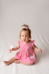 Little girl in a pink dress sits with a comb in his hand on a white background.