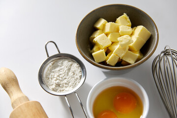 cooking food and culinary concept - rolling pin, butter, eggs, flour and whisk on table