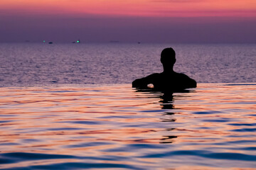 Fototapeta premium Swimming in sunset sunrise. Man swimming in infinity pool. Copy space banner. Hotel business, travel concept, travelling