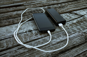 Modern black smartphone charging the battery on a power bank. Rechargeable tech device