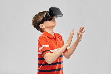 childhood, fashion and people concept - boy in virtual reality headset or vr glasses over grey background