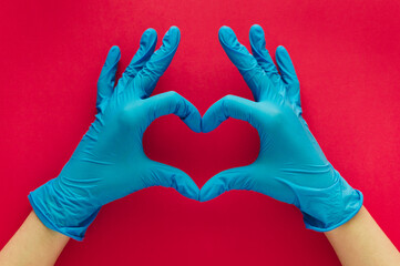 Stock photo of a woman's hands with gloves forming a heart with her fingers on a red background
