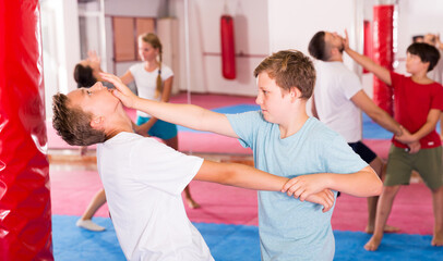Fototapeta na wymiar Kids with adults practicing effective techniques of self-defence in training room