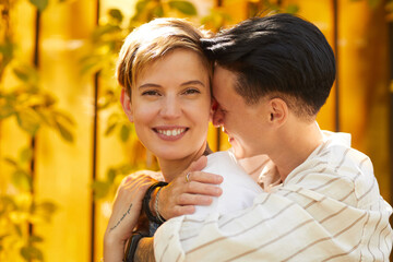 Portrait of young happy woman smiling at camera while her girlfriend embracing her outdoors