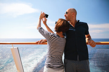 bald man and brunette woman traveling on cruise liner ship and taking pictures from smartphone on balcony  - Powered by Adobe