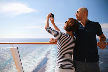 bald man and brunette woman traveling on cruise liner ship and taking pictures from smartphone on...