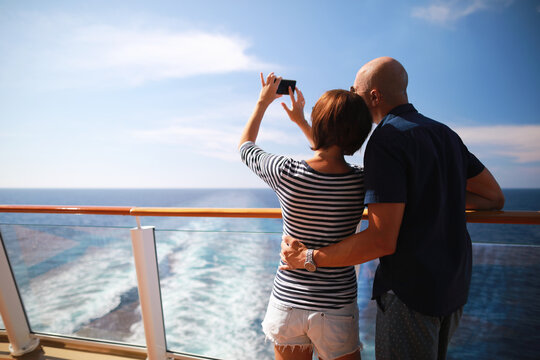 bald man and brunette woman traveling on cruise liner ship and taking pictures from smartphone on balcony 