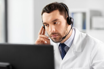 healthcare, medicine and technology concept - male doctor with computer and headset working at...