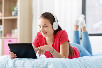 children, technology and communication concept - smiling teenage girl in headphones listening to music on tablet computer at home