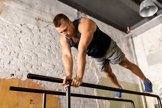 fitness, sport, bodybuilding and people concept - young man doing push-ups or high plank on parallel bars in gym