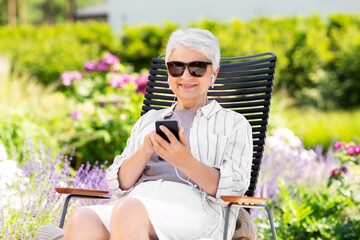 old age, retirement and people concept - happy senior woman in sunglasses with earphones and smartphone listening to music at summer garden