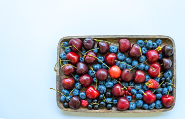 Cherries, blueberries, raspberries, and currants in a wooden plate with copy space