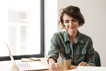 Image of smiling woman writing down notes while working with laptop