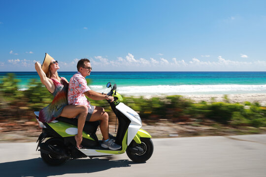 Beautiful young couple in love enjoying and having fun riding on a scooter near beach with beauty and clear water at sea