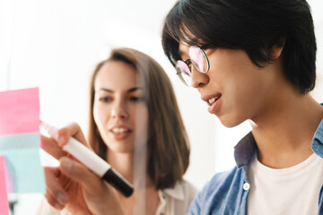 Image of young multinational pleased colleagues using marker pen
