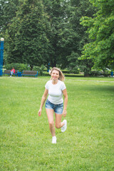 A young girl in denim shorts and a white shirt runs in the park