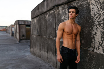 Sexy handsome young man with shirtless torso near old black wall. Sportive healthy man.