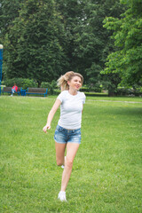 A young girl in denim shorts and a white shirt runs in the park