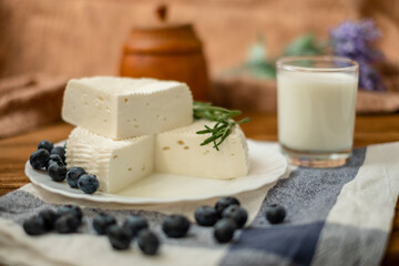 A glass of goat milk and a head of goat milk cheese stand on a wooden table. Cheese at home.