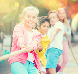 Cheerful children are competing and tug of war on the playground.