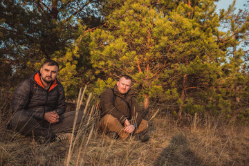 Two friends sitting on the ground in the sunlight and resting after active hike