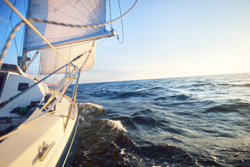 Sailing in the cockpit of a yacht in an open sea at sunrise. Clear blue sky, warm sunlight. Waves...