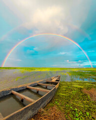 Full rainbow - Empty boat made of wood on a river bank during the rainy season with a rainbow in the background in south asia